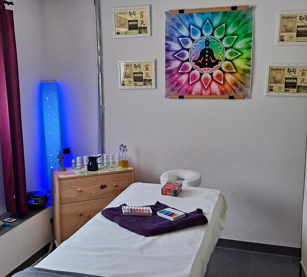 Ein Eindruck des Behandlungsraum  mit einer Massageliege schön hergerichtet und den Bildern an der Wand. Im Hintergrund sieht man eine Blaue Lampe