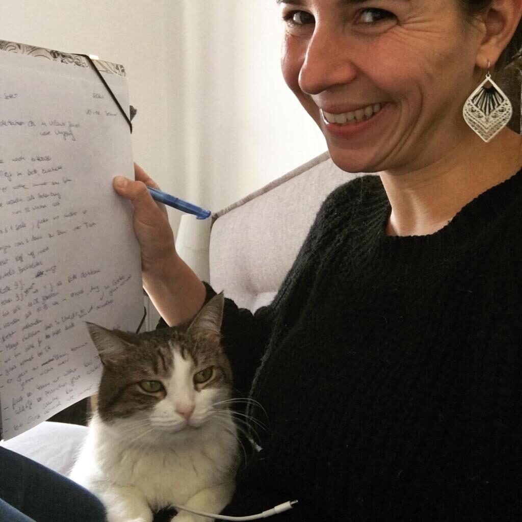 Eine Frau mit einem Block und Stift in der Hand. Auf ihrer Schoss sitzt eine Katze